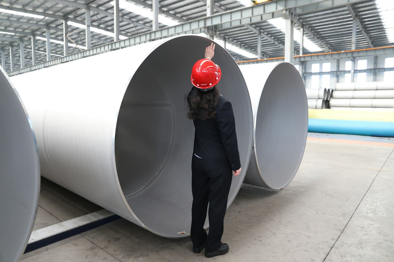 A worker in a hard hat standing beside large-diameter industrial pipes
