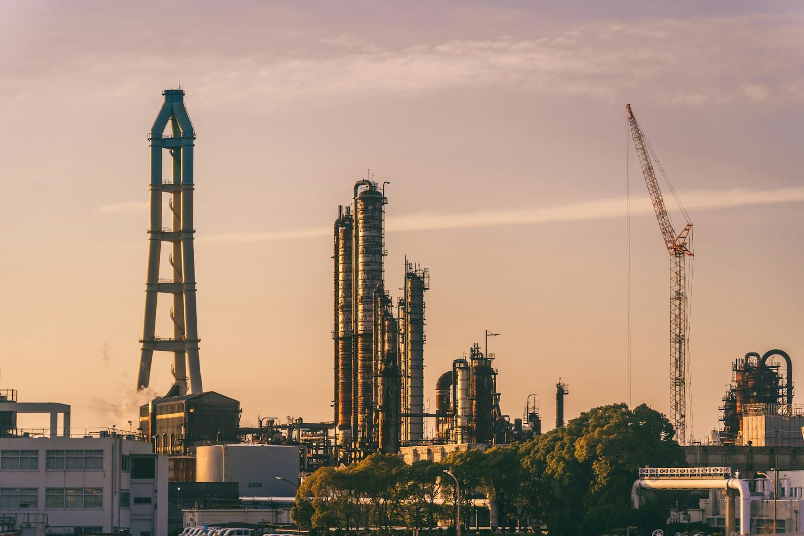 Refinery towers and a construction crane silhouetted against a dusk sky